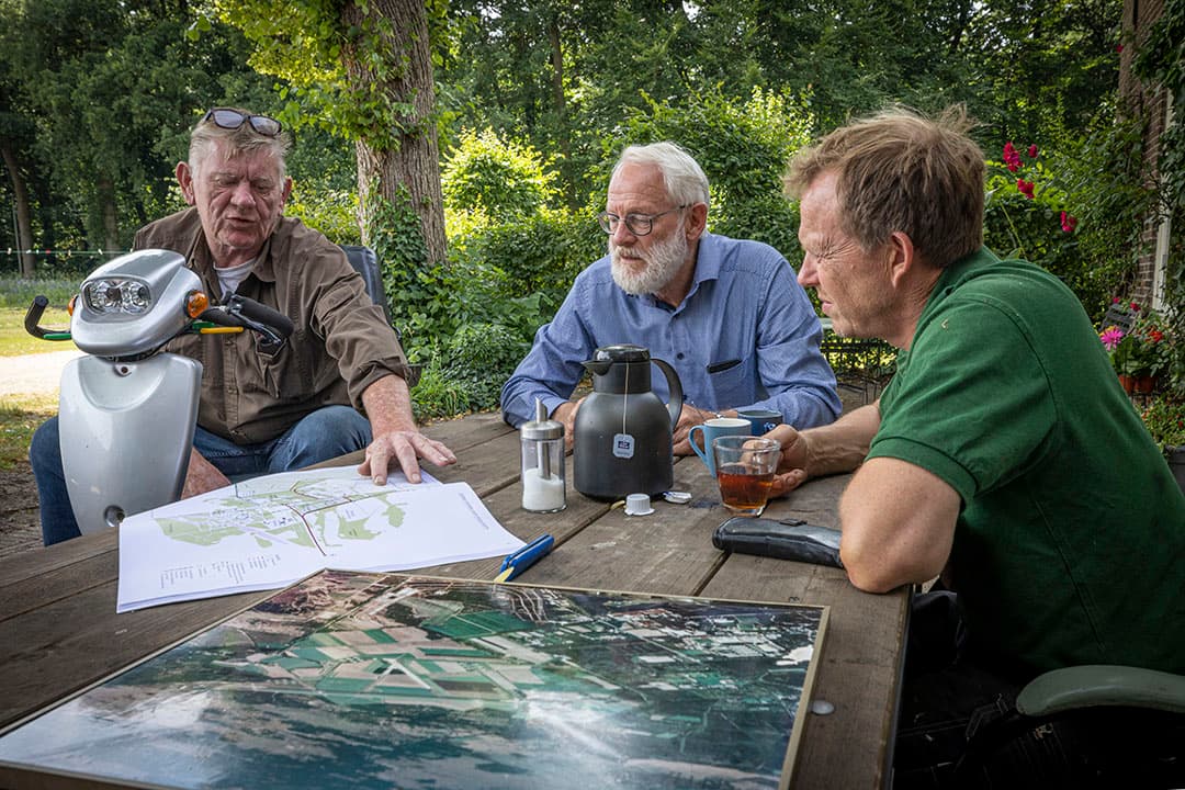 Freek Bruntink, Henny Roelofsen en Arthur van Roekel bij een oude luchtfoto van de vliegbasis met landbouwgronden, en de omgevingsschets met de geplande nieuwe kazerne die ze van het Rijksvastgoedbedrijf hebben ontvangen. Foto's Koos Groenewold