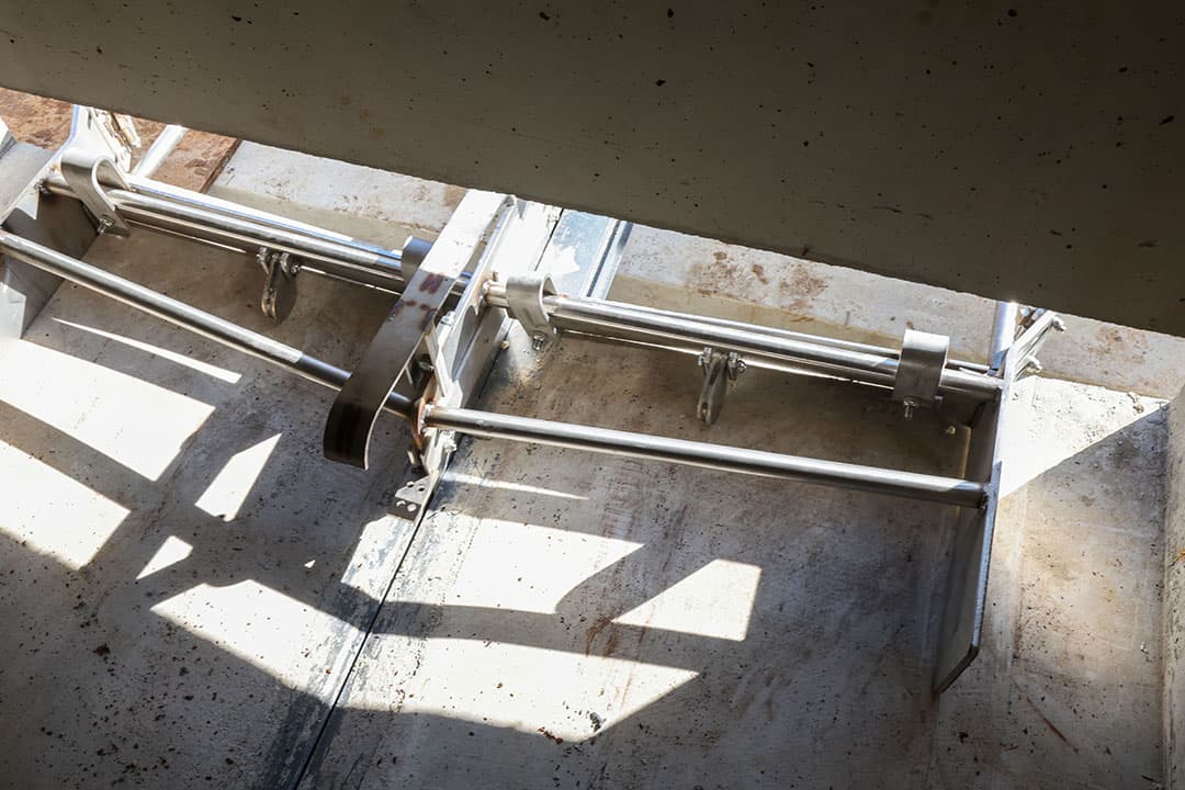 Een roestvaststalen mestschuif klaar voor gebruik in de put onder de roosters. Door de sleuf van de geleider wordt de urine afgevoerd.  Deze ligt onder afschot.