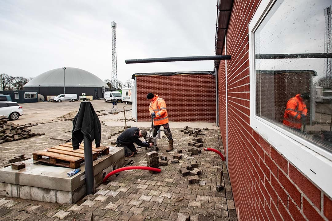 Op de voorgrond de put vanwaar de mest naar de vergister wordt gepompt. Bovenleiding die de stal ingaat om de mestkanalen te spoelen.