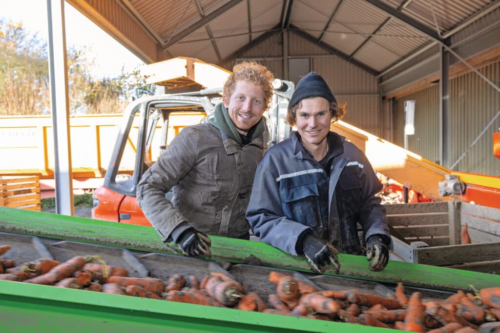 Jan de Koeijer (28, links op de foto) en Niels Heining (31) aan de transportband bij het laden van biologische wortelen. Jan en Niels schakelen het akkerbouwbedrijf van Jans vader Joop (69) en oom Peter (68) om naar biologisch.
