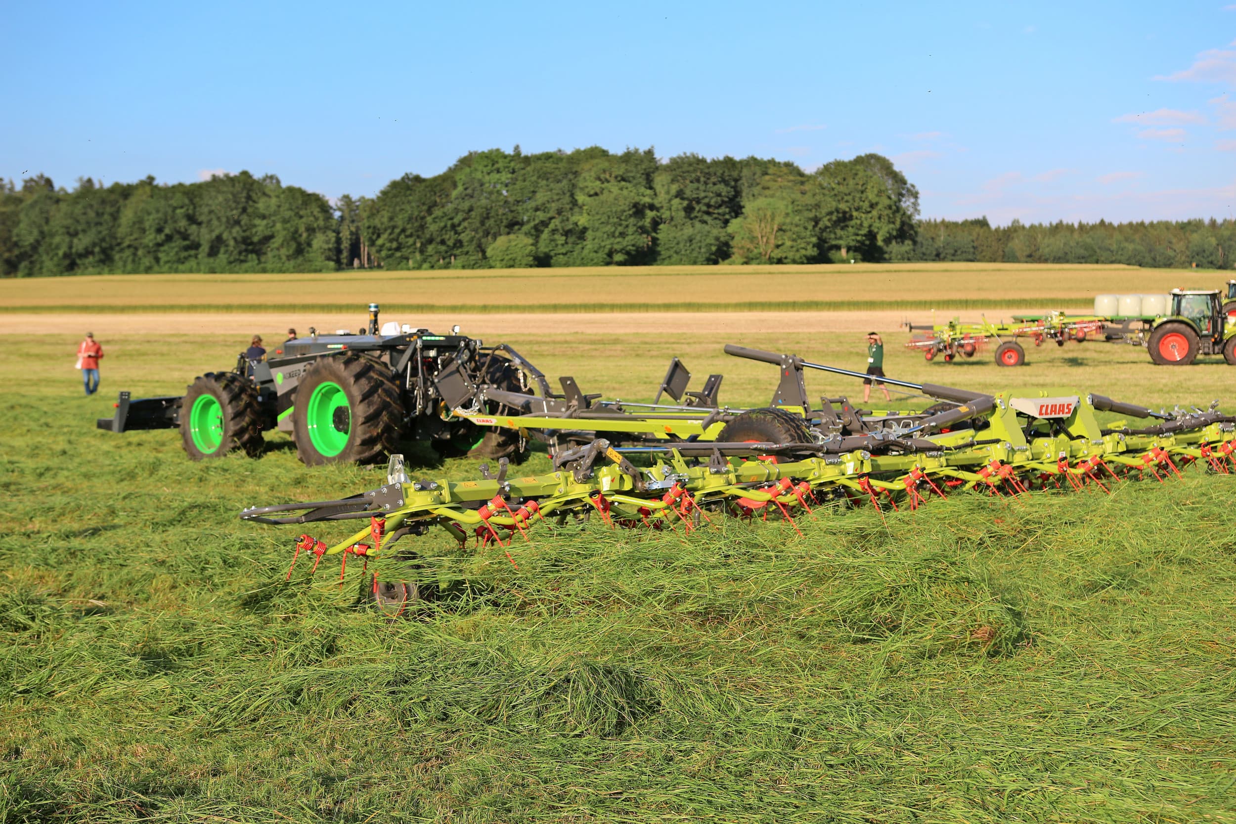 De nieuwe 15,1 meter brede Claas Volto 1500 T in actie op de demonstratie in het Zuid-Duitse Bad Saulgau. Pas als de schudder - dubbelgevouwen - in de lengte opklapt op het transportonderstel, gaan de keurige afschermingen omhoog staan. De transportwielen kunnen optioneel meelopend meesturen in bochten. Volgens Claas wenselijk bij minder stevige graszoden. Er komt ook een iets kleinere Volto 1300 T met twaalf schudrotoren, deze 1500 heeft er veertien. – Foto’s: Bas van Hattum