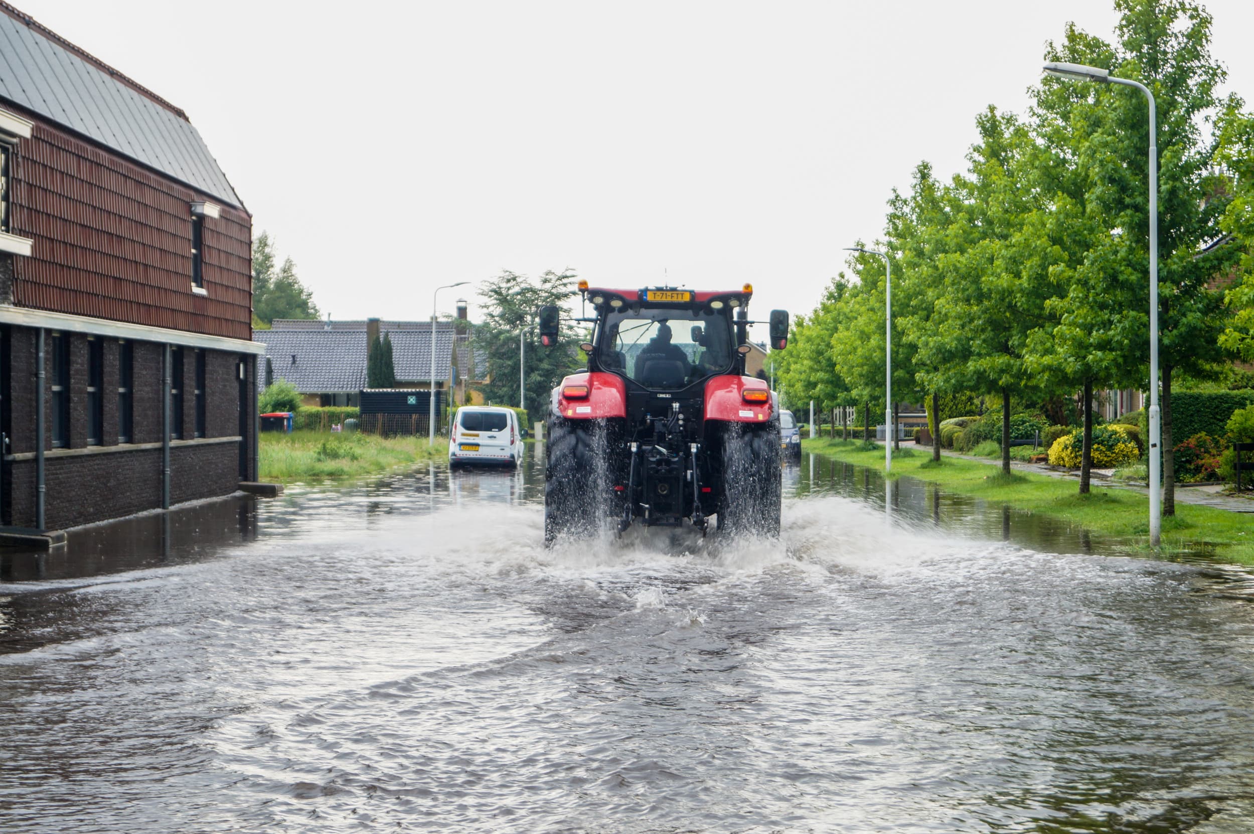 Trekker rijdt door ondergelopen straat in Buitenpost. – Foto: ANP
