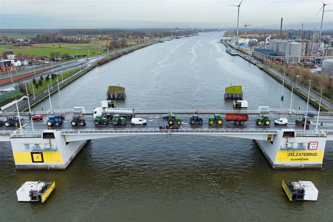 Deze luchtfoto toont boeren die met hun trekkers naar de Zelzatebrug in Zelzate rijden, als protestactie in de havenregio van Gent op donderdag 15 februari 2024. Ze eisen betere voorwaarden om te kunnen groeien, produceren en een fatsoenlijk inkomen te onderhouden. - Foto: ANP