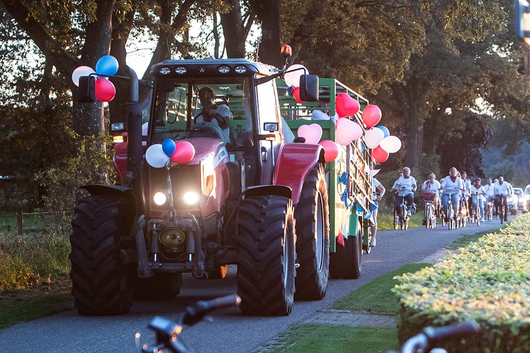 Trekker en veewagen zijn versierd met ballonnen, de hele buurt fietst erachteraan. Zo gaat de stoet op weg naar de boerderij van de bruidegom.