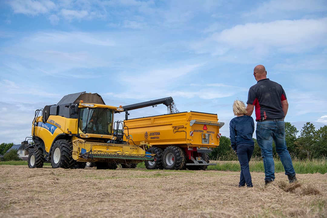 Bram Joostema en zijn dochter Irene kijken toe hoe het Engels raaigras dat al bijna begon door te groeien afgelopen dinsdag nog nét voor de regen van het land kwam. Drogen doen de Joostema’s (Bram, broer Bauke en vader Johannes) zelf. Blij dat het binnen is. Nu wachten op zon voor de tarwe. - Foto: Mark Pasveer