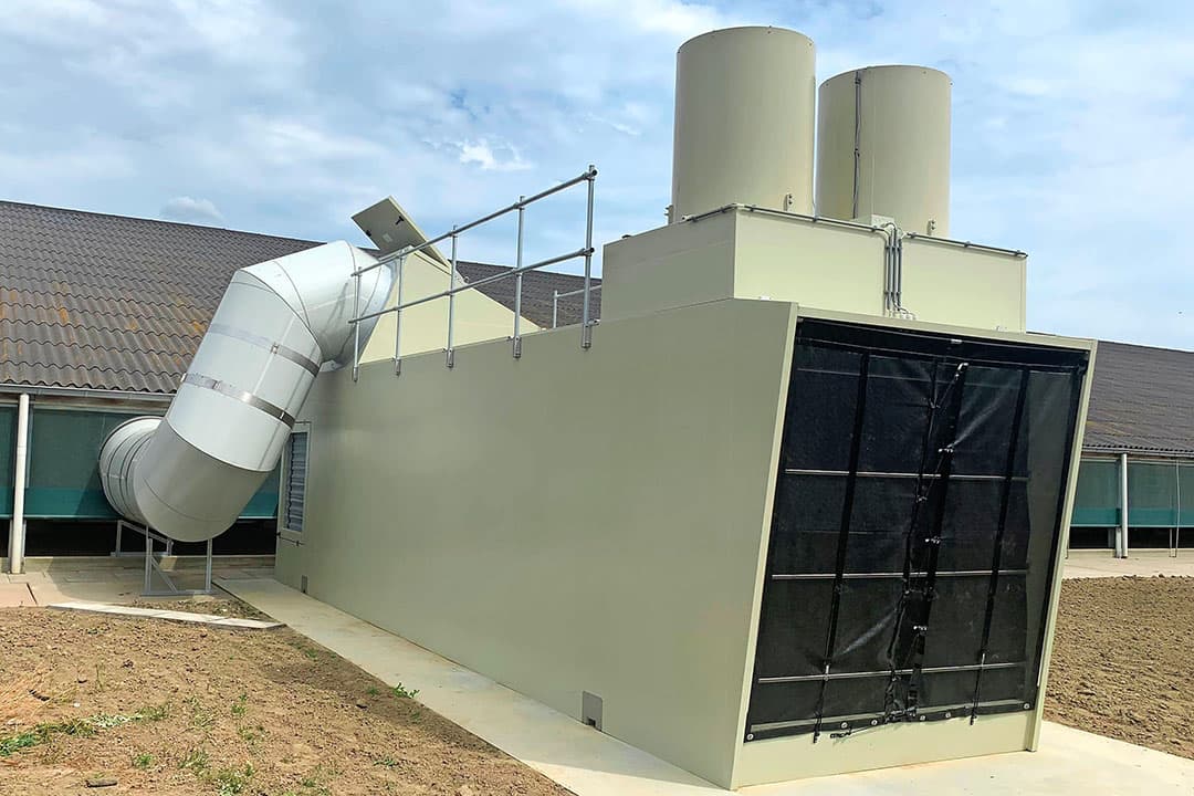 Een van de Eco Air Care-units op een bio-legbedrijf in Zeeuws-Vlaanderen. De dikke buis voert de stallucht aan die via de twee pijpen de unit verlaat. Door een dikke buis tussen unit en de overdekte uitloop (niet zichtbaar) gaat de geconditioneerde buitenlucht de stal in. - Foto: Vencomatic Group