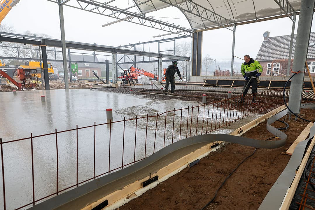 Het beton storten gaat gestaag verder. Goed zichtbaar zijn de buizen die boven het beton uitsteken. Die buizen zorgen straks voor de afvoer van urine in de stal.