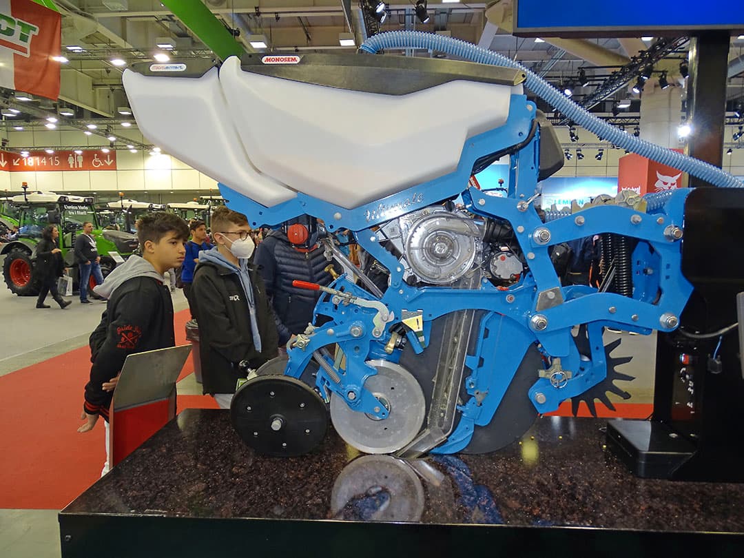 Active Seed Guidance op Monosem-zaaiunit Bij de Franse fabrikant Monosem valt het zaad na verlaten van de zaaischijf niet meer naar beneden door een zaadpijp, maar een soort borstelriem transporteert het tot net boven de grond. Monosem noemt dat ASG, Active Seed Guidance. Voordeel is dat de zwaartekracht geen invloed meer heeft op het zaad. Het versnelt niet langer ongecontroleerd, maar gaat met een constante snelheid naar beneden. Zo realiseert Monosem een nog nauwkeurigere zaadafstand. Tussen de 2 en 18 kilometer per uur ligt de nauwkeurigheid nu boven de 98%. De tweede noviteit is Microsmart. De tweede granulaattank is nu geïntegreerd in de zaadtank. De granulaten kunnen op vier plekken worden gedeponeerd, wel moet de gebruiker bij aankoop reeds kiezen uit twee van die mogelijkheden. Voorheen was de tweede granulaattank altijd apart op de machine gemonteerd, wat de aanblik rommeliger maakte. -Foto's: Martijn Knuivers