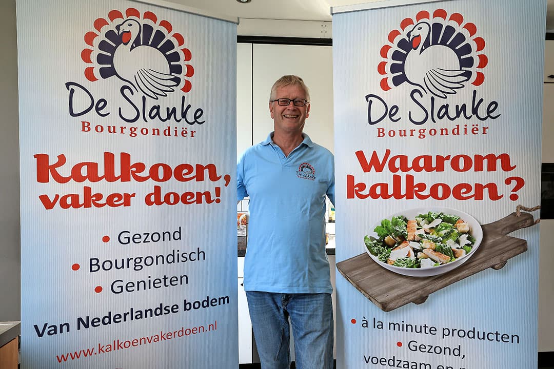 Jo Evers bij campagnemateriaal van De Slanke Bourgondiër. ‘Slanke’ verwijst naar de gezondheidsaspecten: mager vlees en relatief veel eiwit. Met ‘Bourgondiër’ wordt bedoeld dat kalkoen in een Bourgondische levensstijl past.