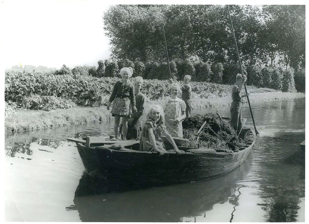 Na het instorten van de visserij legden boeren zich toe op de zogenaamde ‘grove tuinbouw’. Op de achtergrond is daar wat van te zien. Percelen waren niet allemaal even makkelijk met paard of trekker te bereiken, de boot was vaak net zo handig en de jeugd vermaakte zich ermee. - Foto: Misset