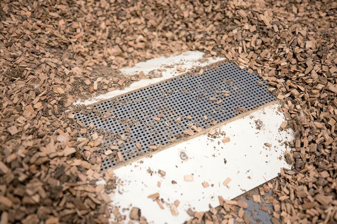 De mestschuifel schuift onder het strooisel door, fijn stof zakt uit het strooisel in de mestschuifel. - Foto: Koos Groenewold