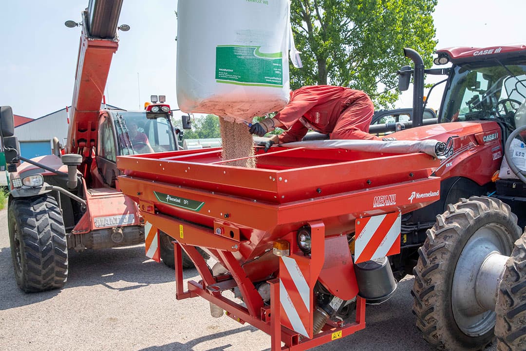Een medewerker van het loonbedrijf snijdt een zak kunstmest open. Achterop de trekker de zaaimachine, zodat in een werkgang de mais de grond in kan, voorzien van bemesting. Begin juni mais zaaien is relatief laat in het noorden van het land. Zoals hier in het Groningse Oudeschans bij veehouder Van Duijnhoven bleef het lang te nat om mais te zaaien. - Foto: Koos van der Spek