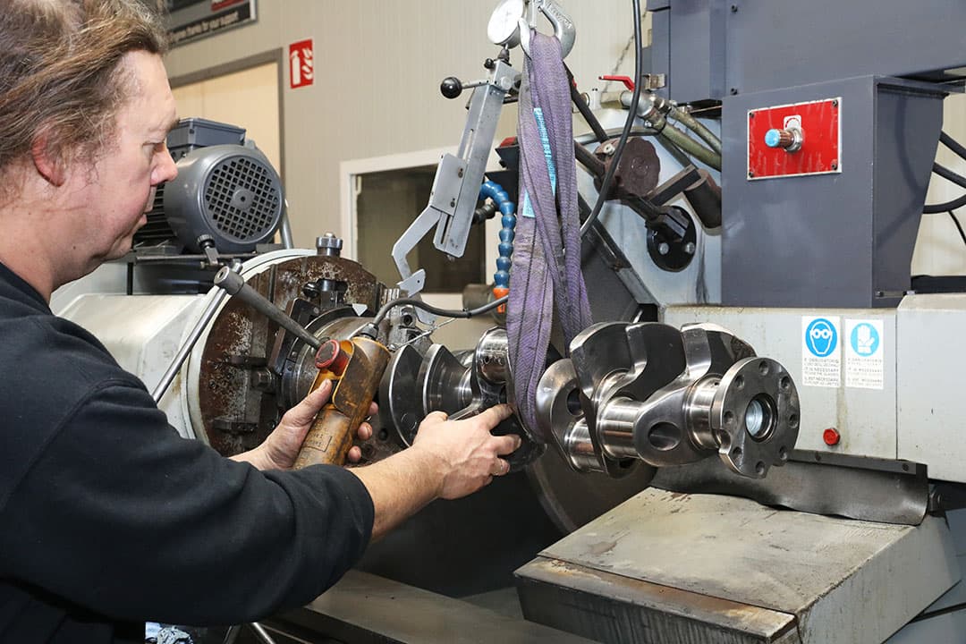 Met deze machine bewerken de techneuten (beschadigde) krukassen. De as draait tegen een draaiende slijpsteen aan de achterzijde van de machine. Tijdens het slijpen is het belangrijk om continu te meten.