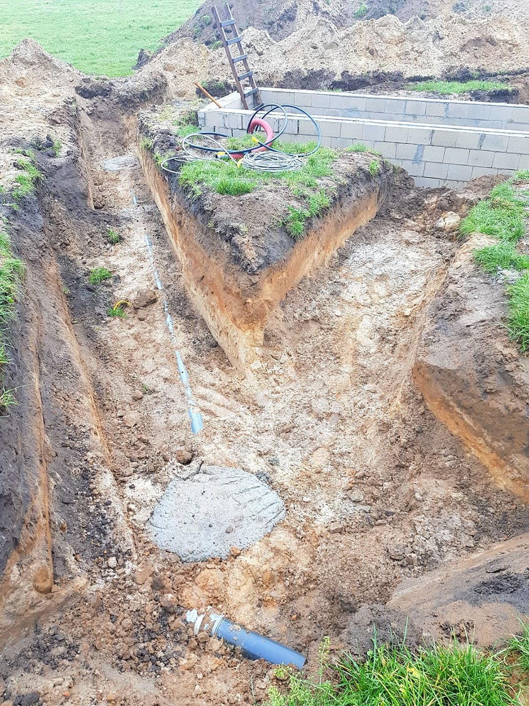 Hier wordt het eerste deel van de buitenrand met behulp van een kraan op z n plek gezet. Net als bij de spanten is ook dit materiaal niet hagelnieuw. Smale koos voor oude sleufsilowanden. Dit wordt overigens geen buitenmuur. De wand steekt niet ver boven de grond uit en is vooral bedoeld om het beton  op te sluiten . Er komt straks een aarden wal tegenaan.