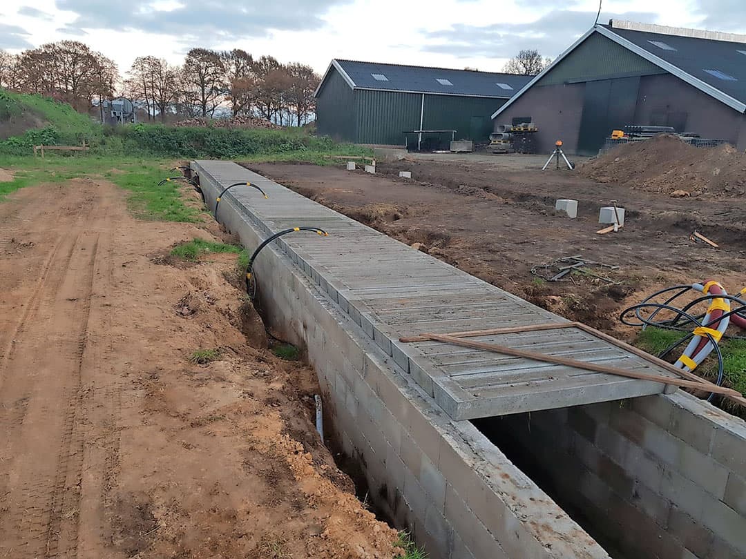De 2 grijze, geïsoleerde tyleen leidingen die hier langs de put van de kalverstal lopen, zijn bedoeld voor drinkwater. Eentje ervan is voor de waterbakken buiten. De rode mantelbuis is er voor krachtstroom en gewone stroom. Ook loopt er een internetkabel doorheen.