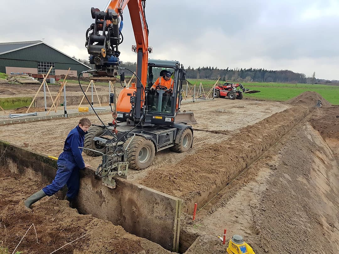 De palen aan de zijkanten van de mestput/roostervloer zijn precies gesteld en worden door houten balken ondersteund. Die balken worden pas na het beton storten weggehaald. Tussen de betonnen poeren (links) en de mestput is ruimte voor 3 strohokken. Links van de poeren komen de kalveriglo s te staan.
