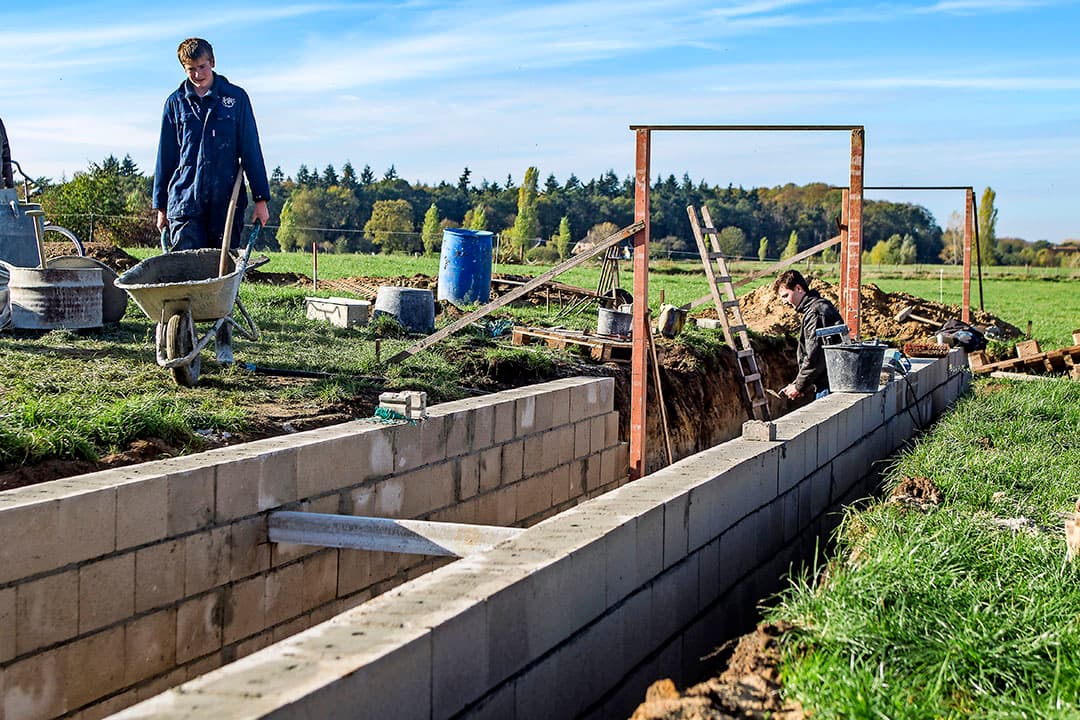 Ondertussen draait de betonmolen door. Op de achtergrond is de ligboxenstal te zien.