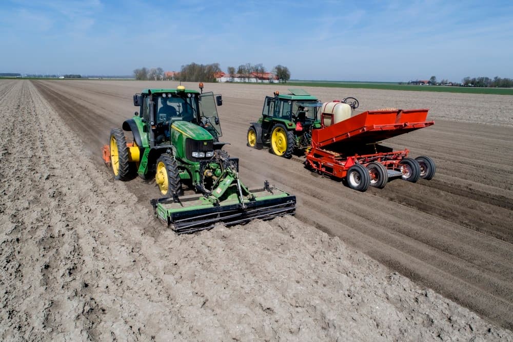 Daarachter hangt een zaaibedcombinatie met ganzenvoeten die het land intensief bewerken en vlaktrekken. De Poolse chauffeur maakt uienland klaar voor biologische bedrijven Twisk uit Biddinghuizen en van Andel uit Zeewolde.