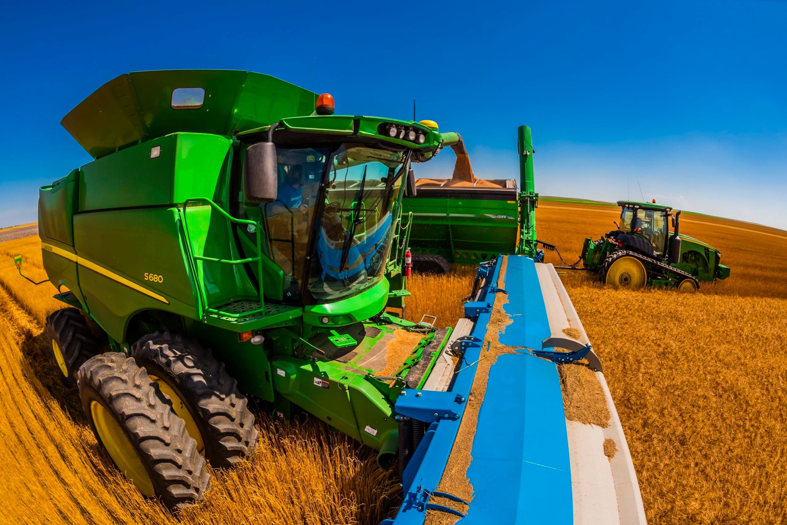 Combine harvestors unload their grain into a grain wagon pulled by a tractor during the wheat harvest, Schields & Sons Farming, Goodland, Kansas USA.