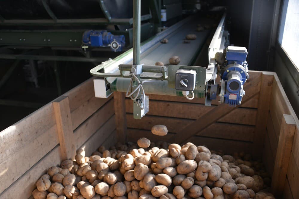 Onder de afvoerbuizen van loof en stof staat een geluidsarmecompressor die zorgt voor de luchtdruk, om de aardappelen op de juiste plaats van de band te blazen.
