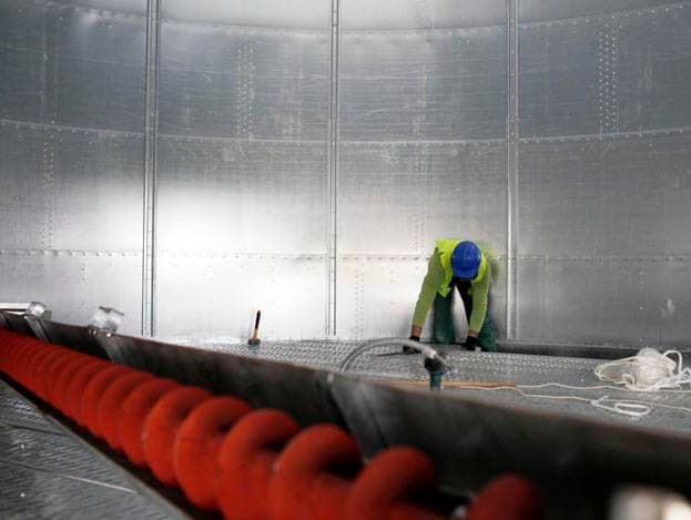 De laatste hand aan de vloer wordt gelegd. Op de voorgrond de veegvijzel. Hiermee wordt het graan vanuit de zijkanten naar het midden getransporteerd.