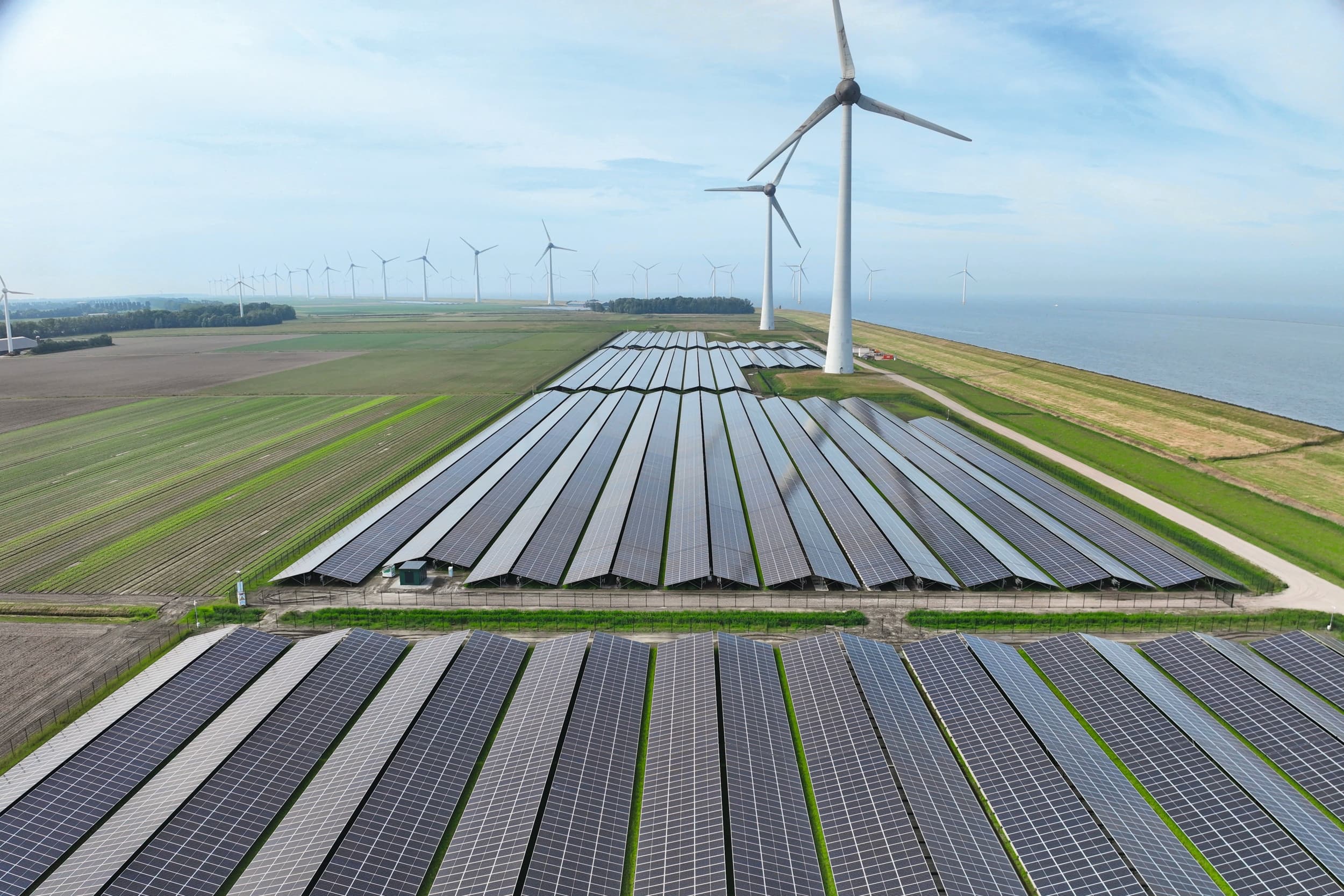 Het zonnepark in de Noordoostpolder is langgerekt en vormt samen met de windmolens die er al stonden een energielandschap. Foto: Ampyr