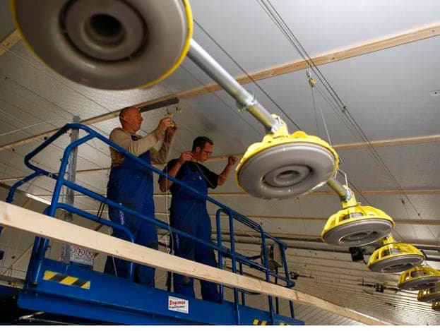 De bouwvakkers monteren de voerlijnen met lieren aan het plafond van de nieuwe stal. In het midden van de stal kan de pluimveehouder de voer- of waterlijnen per lijn bedienen.