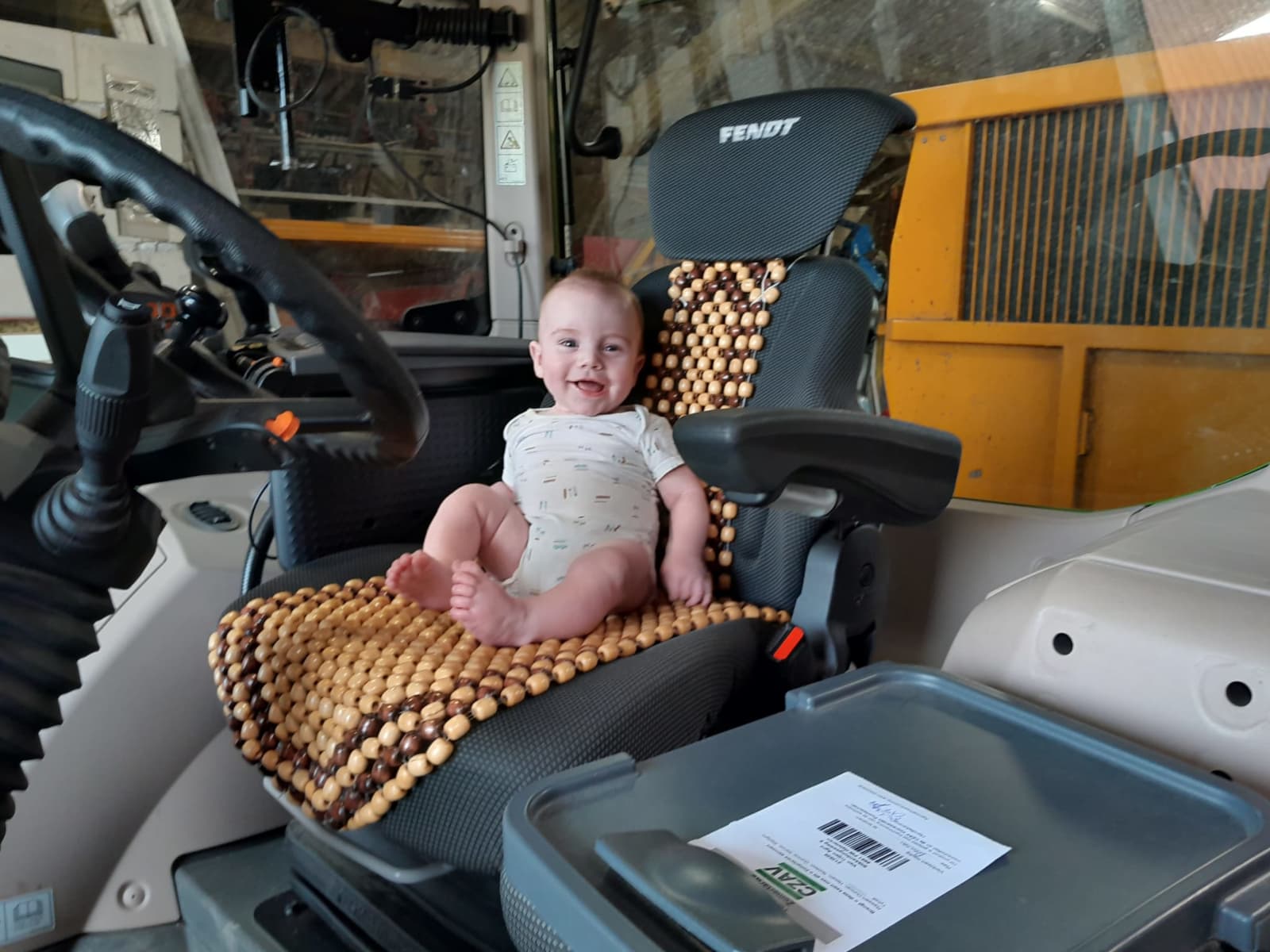 Tim is op de foto nog nog geen half jaar en kan net een beetje zitten en doet dat nu voor het eerst zelfstandig in de Fendt 516. Tim wil nu al de zomertarwe van vader Eric-Jan van Trijen wegbrengen van Halsteren naar de CZAV in Dinteloord. Veiligheid voorop dus en eerst maar even een veiligheidshesje aan. – Foto: Eric-Jan van Trijen