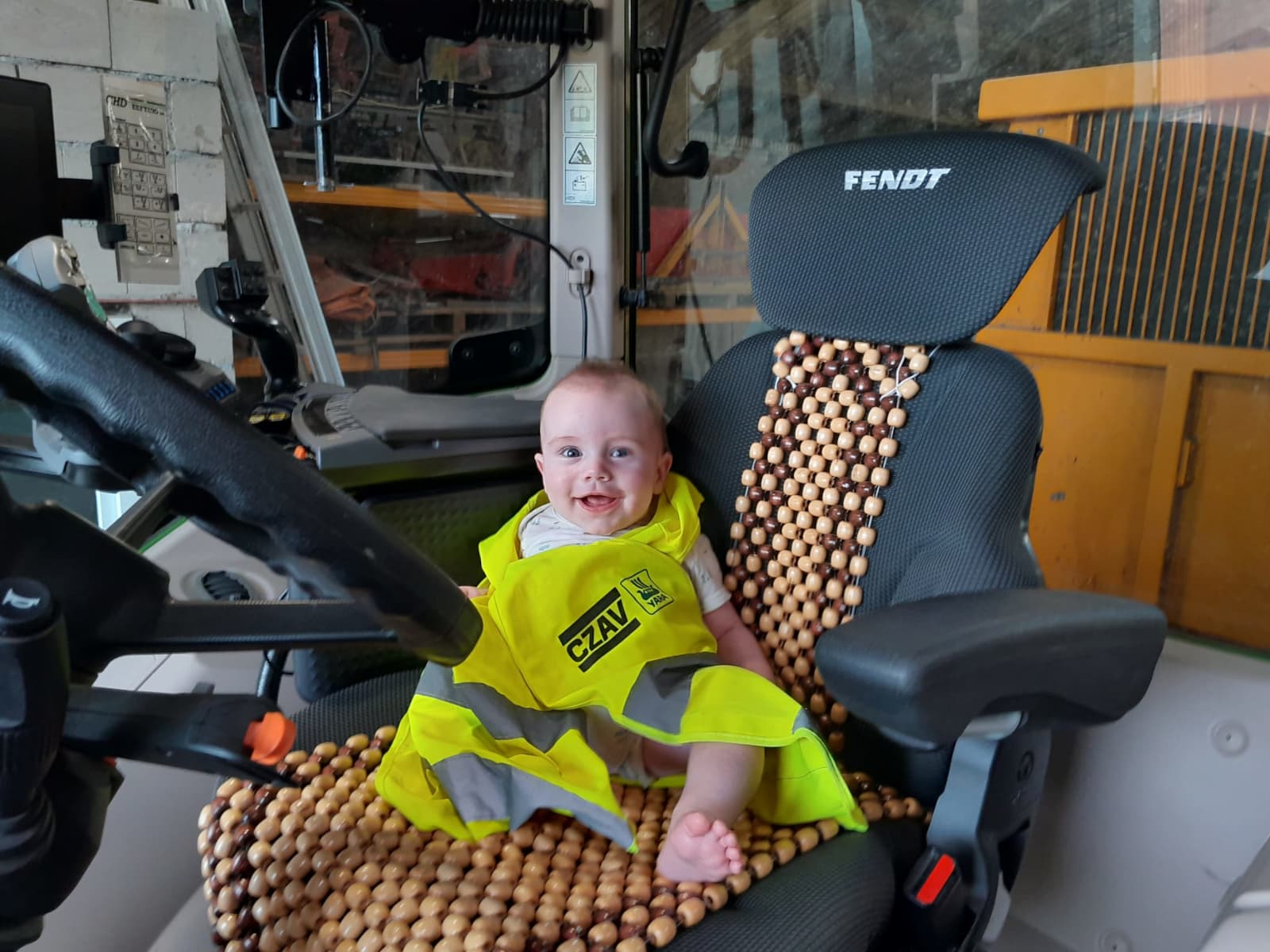 Tim is op de foto nog nog geen half jaar en kan net een beetje zitten en doet dat nu voor het eerst zelfstandig in de Fendt 516. Tim wil nu al de zomertarwe van vader Eric-Jan van Trijen wegbrengen van Halsteren naar de CZAV in Dinteloord. Veiligheid voorop dus en eerst maar even een veiligheidshesje aan. – Foto: Eric-Jan van Trijen