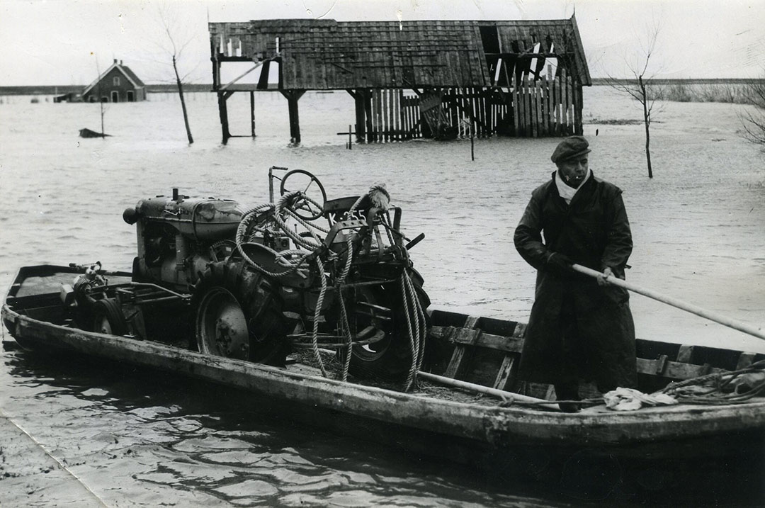 Een trekker die onder water stond, wordt per boot naar een smid gebracht. De hoop is dat er nog wat te repareren valt.